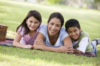 Mother and two young children outdoors in park with picnic smiling (selective focus)
