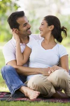 Couple sitting outdoors in park being affectionate and smiling (selective focus)