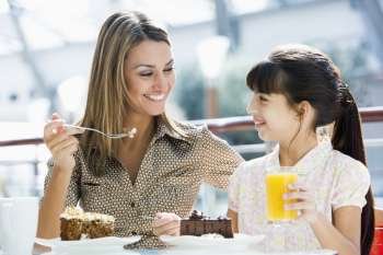 Mother at restaurant with daughter eating dessert and smiling (selective focus)