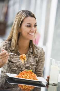 Woman at restaurant eating spaghetti and smiling (selective focus)