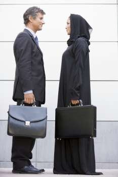 Two businesspeople standing outdoors with briefcases smiling