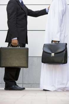 Two businessmen standing outdoors with briefcases
