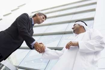 Two businessmen outdoors by building shaking hands and smiling (high key/selective focus)