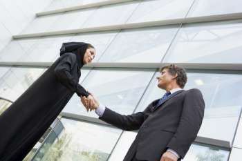 Two businesspeople standing outdoors by building shaking hands and smiling (selective focus)