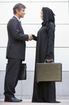 Two businesspeople outdoors shaking hands and smiling