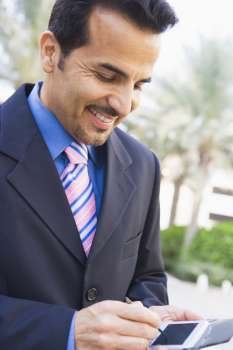 Businessman outdoors using personal digital assistant and smiling (high key/selective focus)