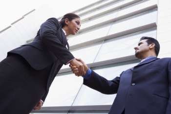 Two businesspeople outdoors by building shaking hands (high key/selective focus)