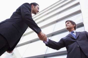 Two businessmen outdoors by building shaking hands (high key/selective focus)