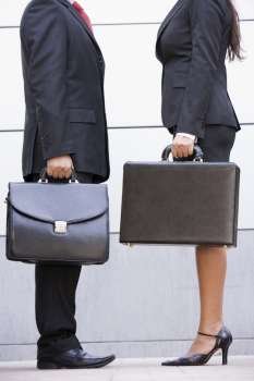 Two businesspeople standing outdoors holding briefcases