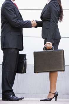 Two businesspeople standing outdoors holding briefcases and shaking hands