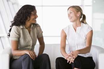 Two businesswomen sitting indoors talking and smiling (high key/selective focus)