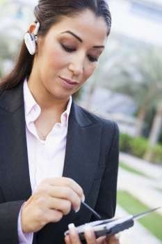 Businesswoman outdoors wearing headset and using personal digital assistant (selective focus)