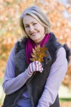 Woman outdoors at park holding leaves in hand smiling (selective focus)