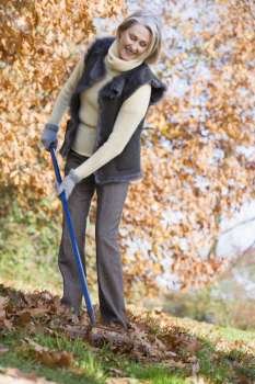 Woman outdoors raking leaves and smiling (selective focus)
