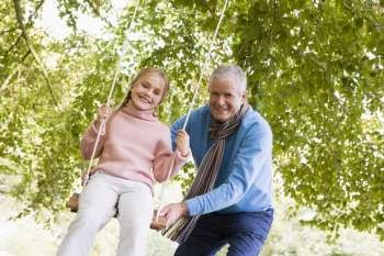 Grandfather pushing granddaughter on swing and smiling (selective focus)