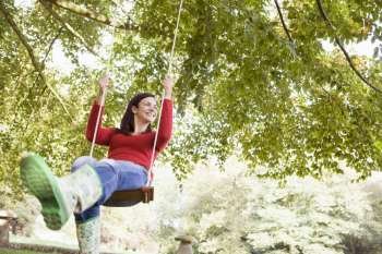 Woman outdoors swinging on tree swing and smiling (selective focus)