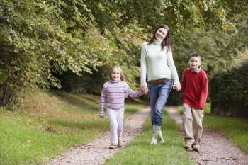 Mother and two children walking on path outdoors smiling (selective focus)