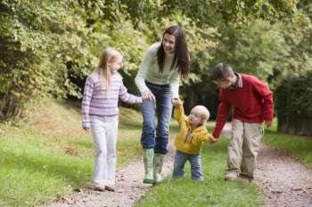 Mother and three young children walking on path outdoors smiling
