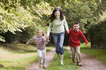 Woman outdoors with two young children walking on path holding hands and smiling (selective focus)
