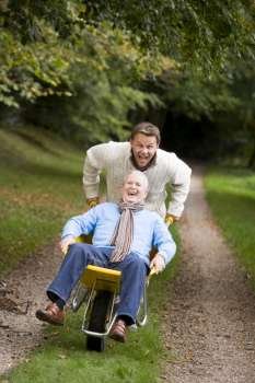 Son pushing senior father in wheelbarrow