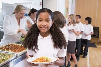 Students in cafeteria line with one holding up her healthy meal looking at camera (depth of field)