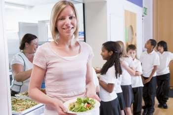 Students in cafeteria line with teacher holding her healthy meal and looking at camera (depth of field)