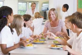 Students sitting at cafeteria table eating lunch with teacher