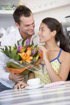 Young man giving a bouquet of flowers to a young girl sitting at a table