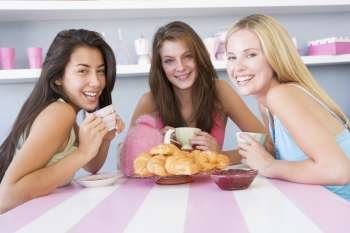 Three young woman sitting at a table having tea and a snack