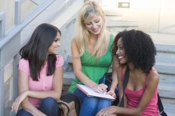 Three women sitting on staircase outdoors writing in notebook