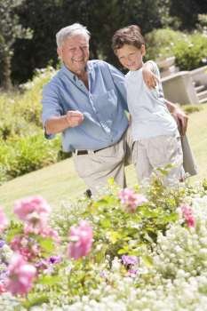 Grandfather and grandson outdoors in garden pointing at plants and smiling