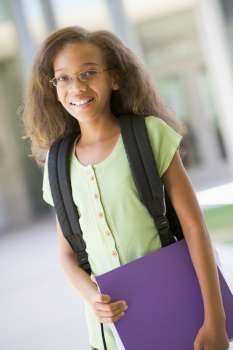 Student standing outside school holding binder and smiling (selective focus)