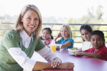 Teacher sitting at table outdoors with students eating lunch in background (depth of field)