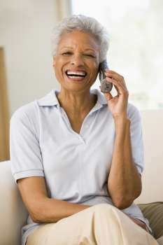 Woman sitting in living room using telephone and smiling