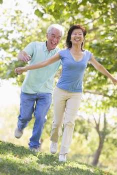 Couple running outdoors in park by lake smiling