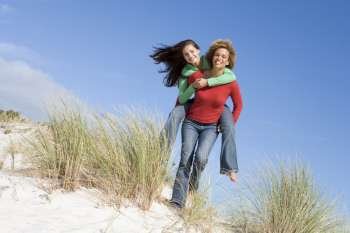 Young woman giving piggyback ride to her friend on a sand hill
