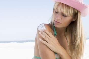Woman on beach applying sunblock lotion to her shoulder