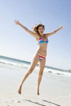 Woman in a two piece bathing suit jumping on a beach