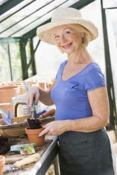 Woman in greenhouse putting soil in pot and smiling