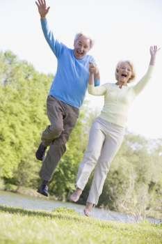 Couple jumping outdoors at park by lake smiling