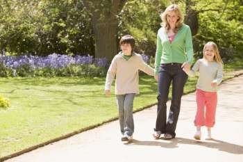 Mother and two young children walking on path holding hands smiling