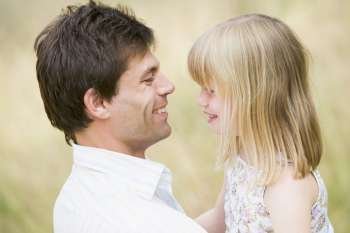 Father holding daughter outdoors smiling