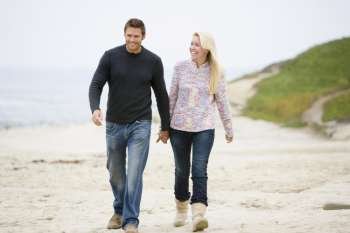 Couple walking at beach holding hands smiling