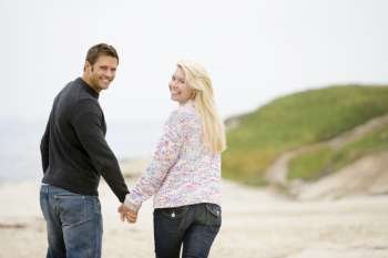 Couple walking at beach holding hands smiling
