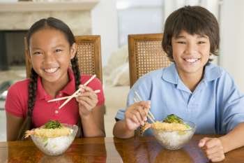Two young children eating Chinese food in dining room smiling