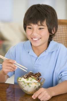Young boy in dining room eating chinese food smiling