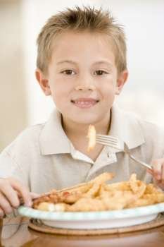 Young boy indoors eating fish and chips smiling