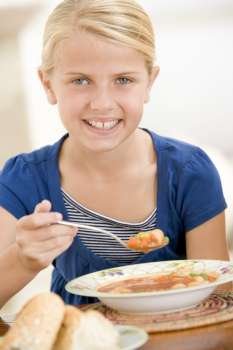 Young girl indoors eating soup smiling