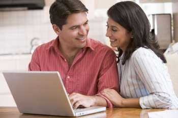 Couple in kitchen using laptop and smiling