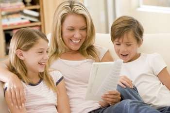Woman and two young children in living room reading book and smiling